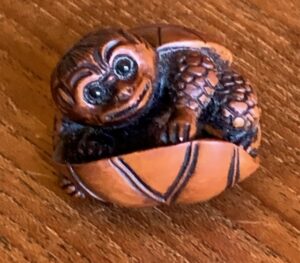 Kappa netsuke holding onto lotus leaf like a couched in a boat.