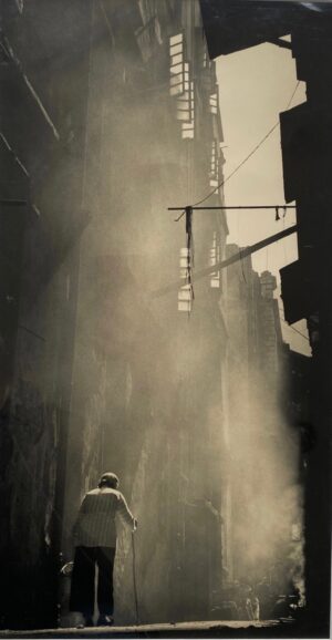 Fan Ho photograph of a woman with a walking stick in a Hong Kong side street